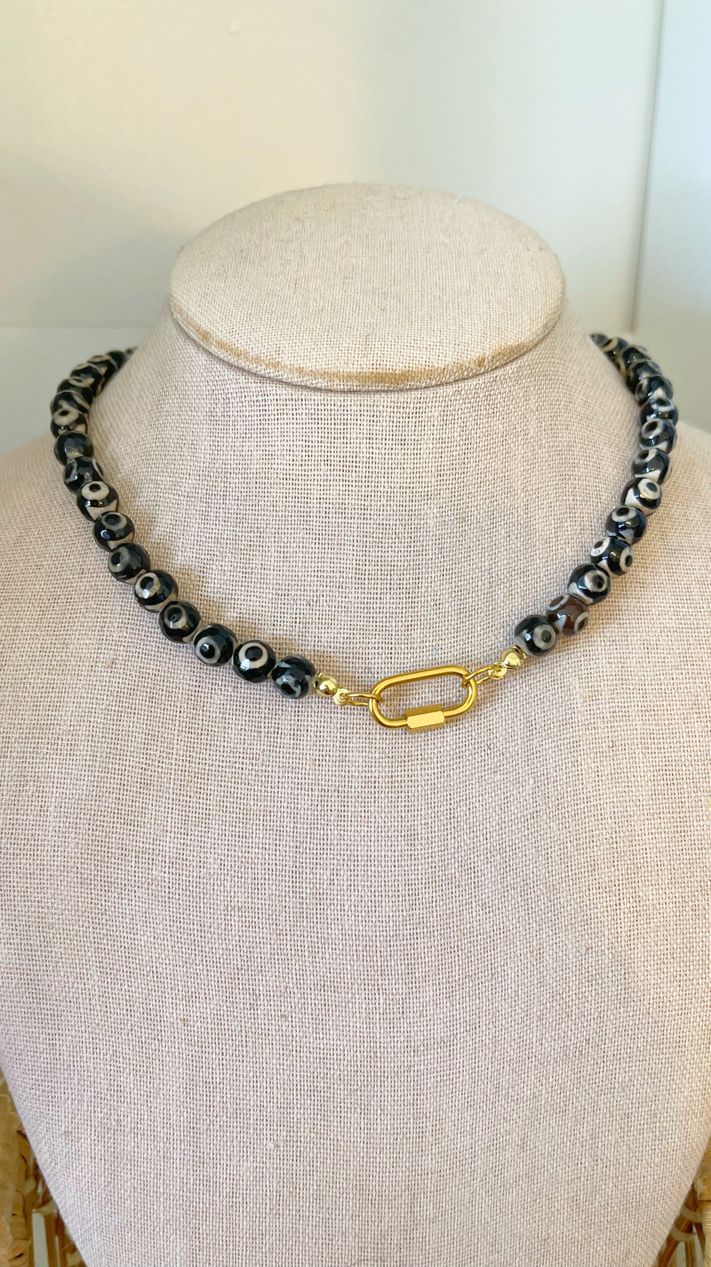 Necklace with black beads and gold clasp on a mannequin bust.