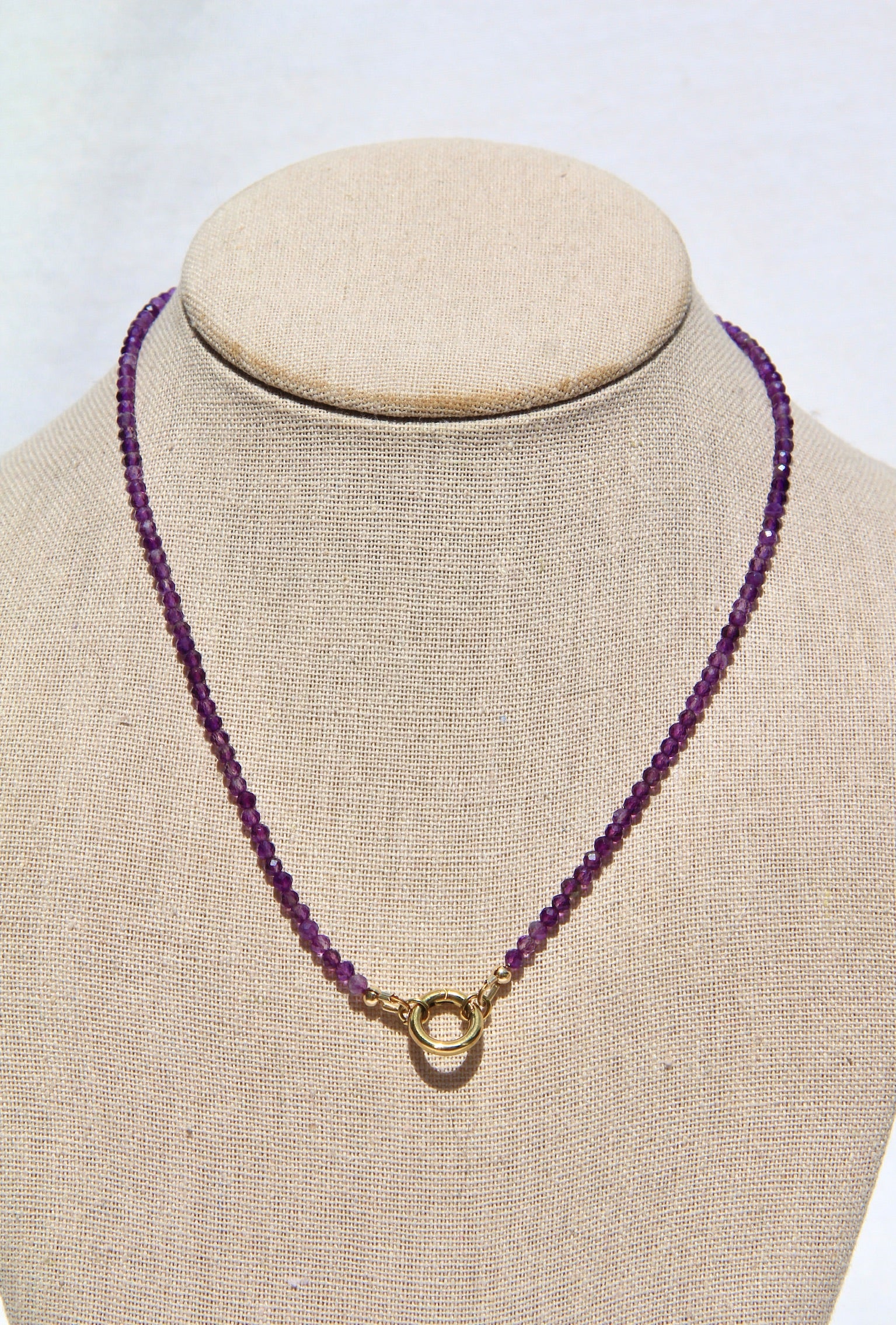 Purple beaded necklace with a gold clasp on a mannequin bust against a white background
