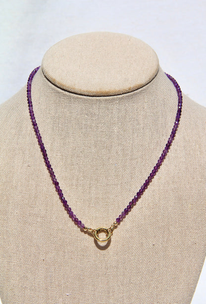 Purple beaded necklace with a gold clasp on a mannequin bust against a white background