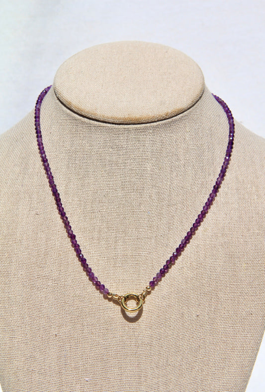 Purple beaded necklace with a gold clasp on a mannequin bust against a white background