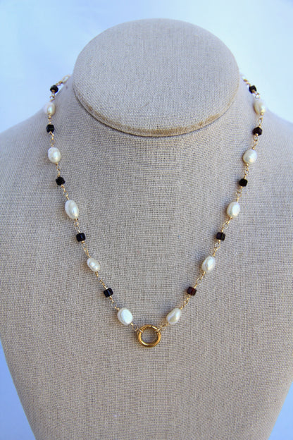 Necklace with pearls and black beads on a mannequin bust against a light blue background
