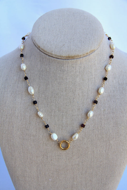 Necklace with pearls and black beads on a mannequin bust against a light blue background