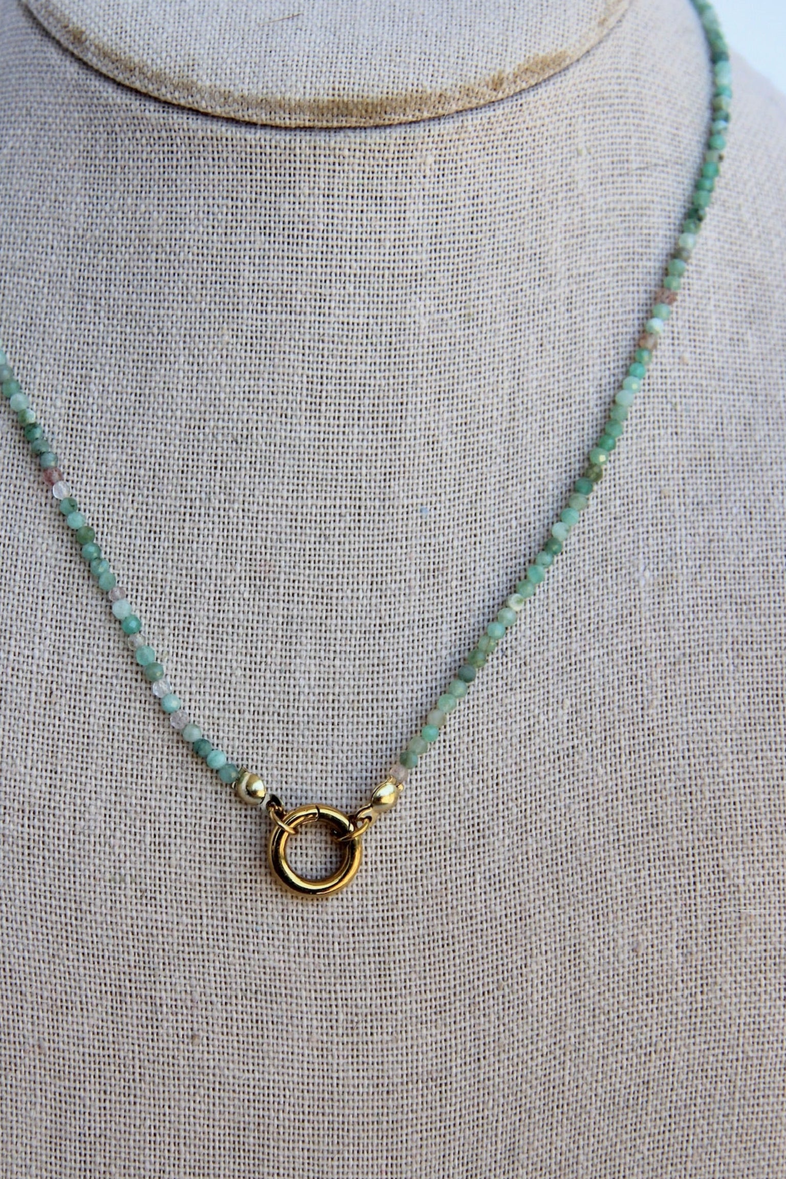 Necklace with green beads and gold clasp on a mannequin bust.