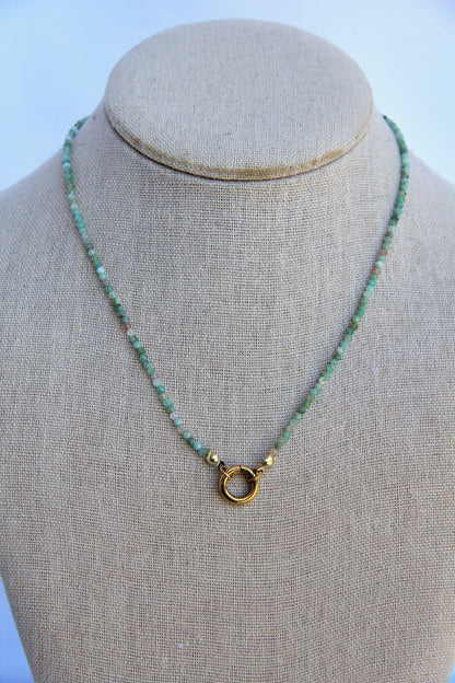 Necklace with green beads and a gold clasp on a mannequin bust against a light blue background